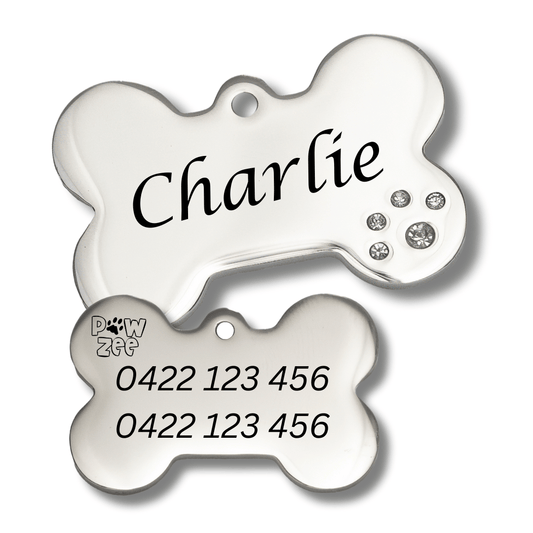Two silver bone-shaped pet ID tags with 'Charlie' engraved on the top and a contact number on the bottom, adorned with small zirconia gemstone crystals.