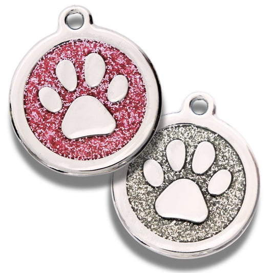 Two round designer dog tags with a paw print in the center, one with a pink glitter background and the other with a silver glitter background.