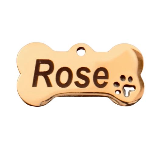A rose gold stainless steel dog name tag in the shape of a bone with the name 'Rose' engraved on it, featuring a paw print cut out at the end.