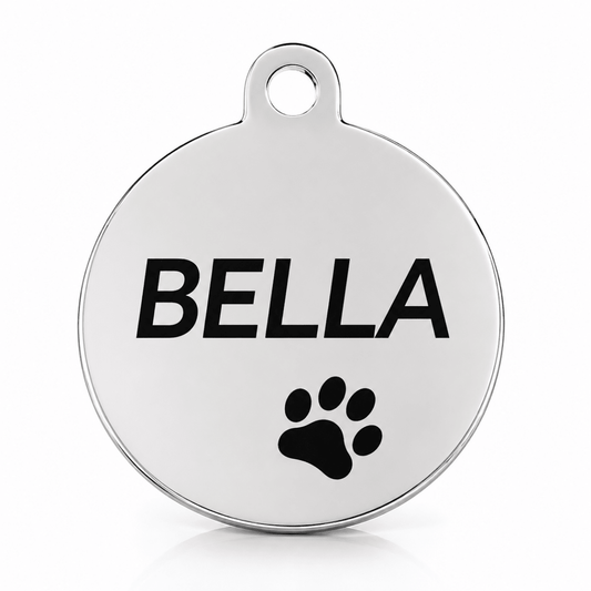 A round silver metal pet ID tag with a hanging loop at the top, featuring the name 'BELLA' engraved in bold black letters and a black paw print below it, shown on a clean white background.